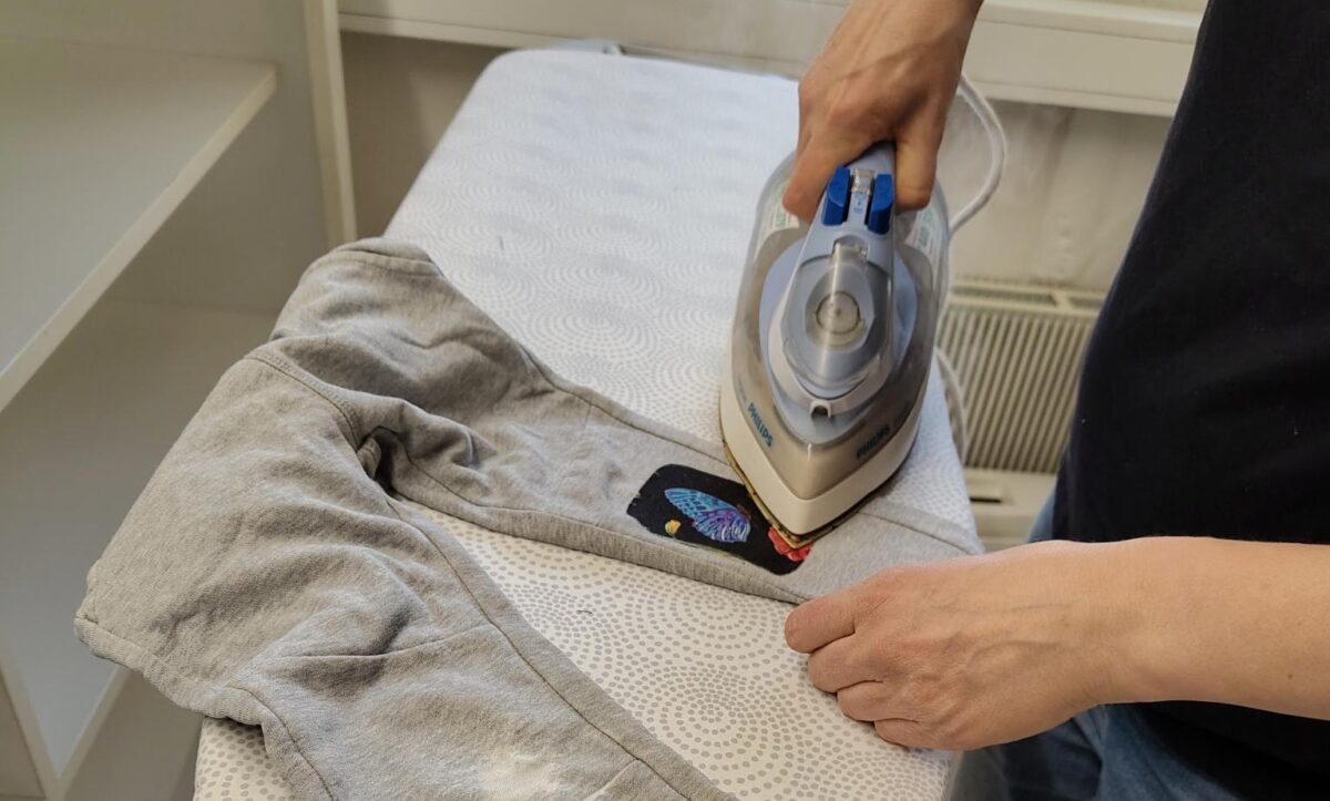 Participant ironing decorative patches onto worn grey sweatpants during a CARE clothing repair activity in Tampere.
