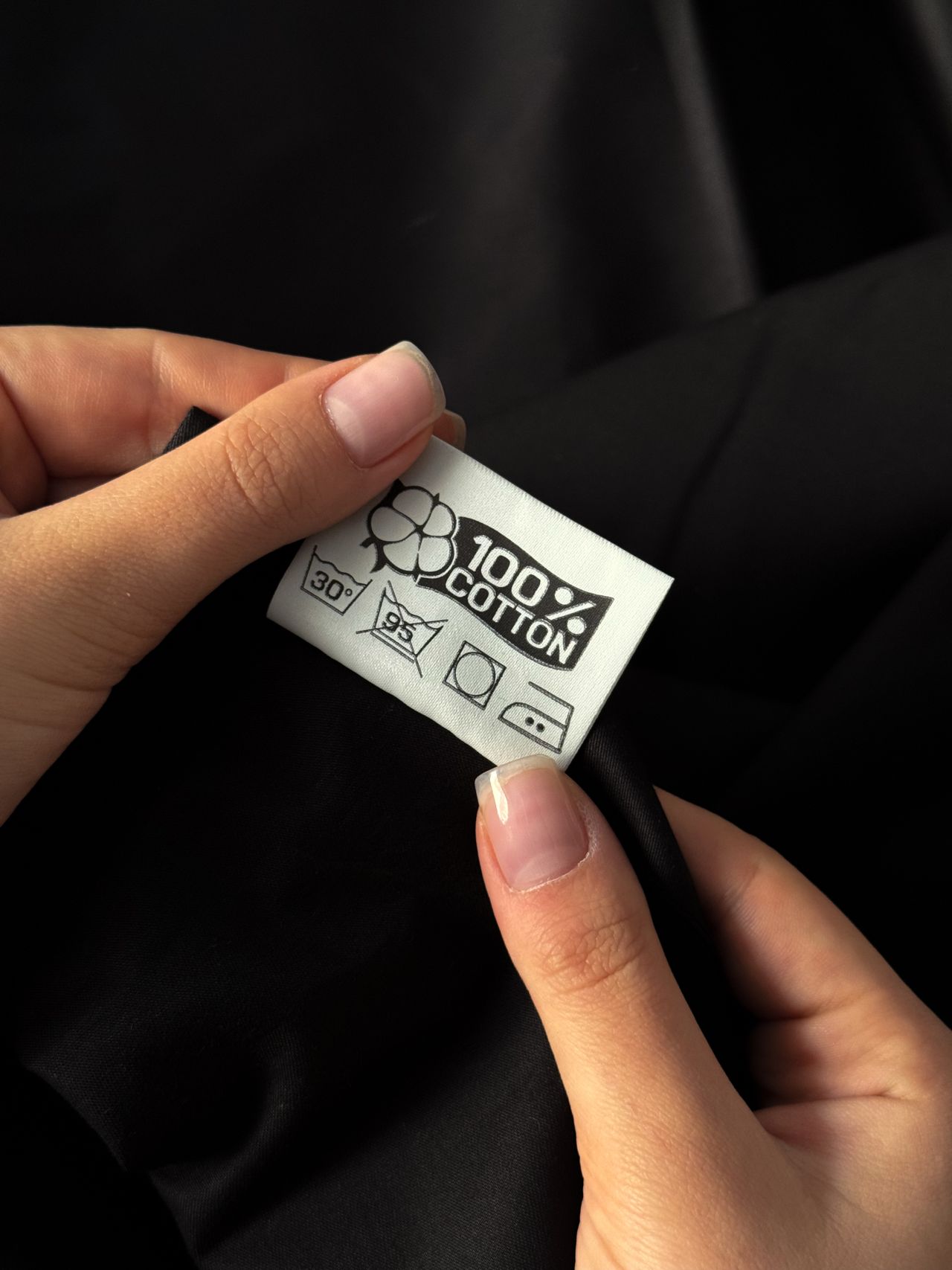 Hands holding a care label on a black cotton garment