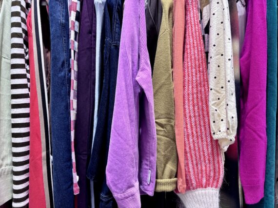Colourful shirts, trousers and knitwear hanging on a clothes rail at the Berlin CARE clothing workshop.